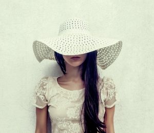 Stylish woman in a white hat & dress posing for a photo.